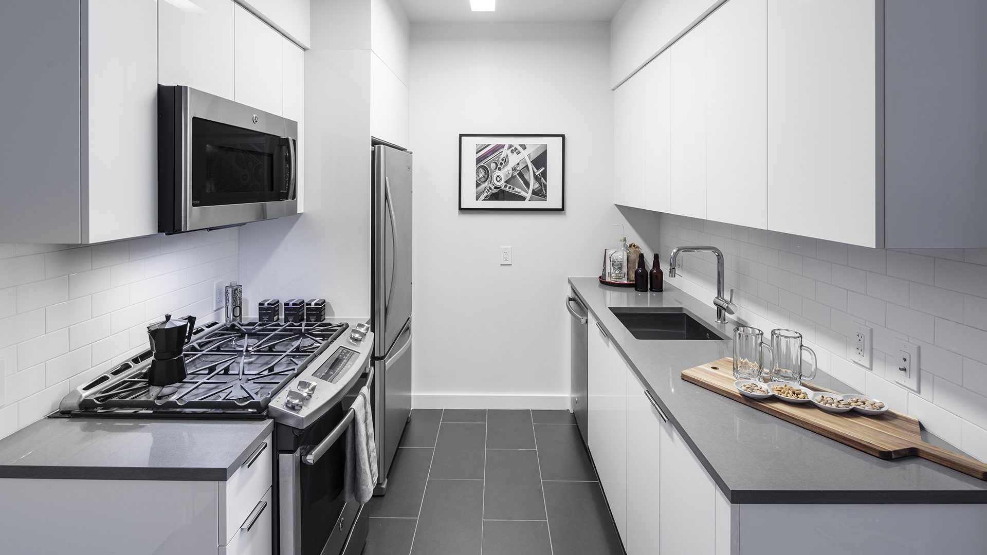 An image of a kitchen featuring brand new stainless steel appliances, grey flooring, and white countertops.
